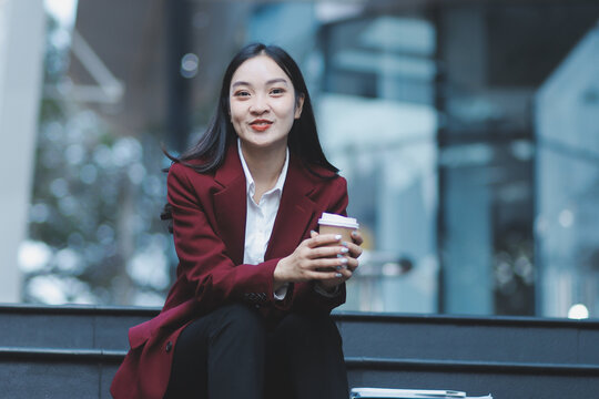 Focused woman in blazer types on laptop outdoors. Urban professional works remotely on stairs. She uses modern tech for business and connection.