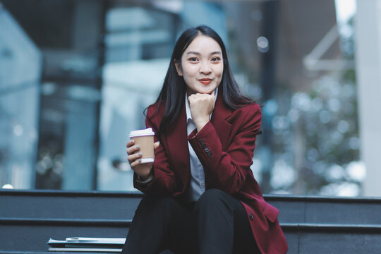 Focused woman in blazer types on laptop outdoors. Urban professional works remotely on stairs. She uses modern tech for business and connection.