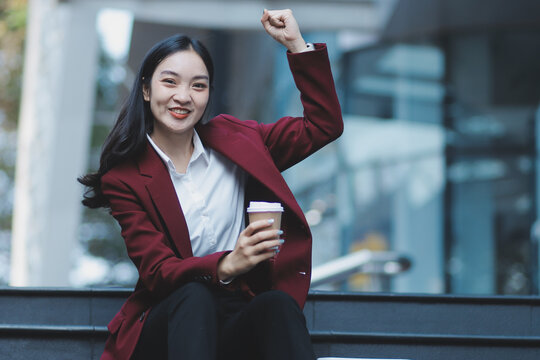 Focused woman in blazer types on laptop outdoors. Urban professional works remotely on stairs. She uses modern tech for business and connection.