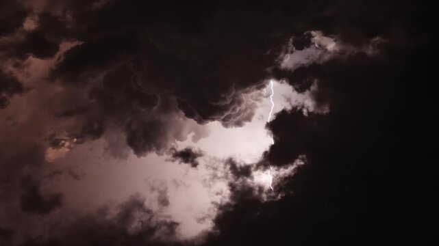 Ominous time lapse of dark, heavy storm clouds rolling through the sky with a moody, reddish purple glow at night