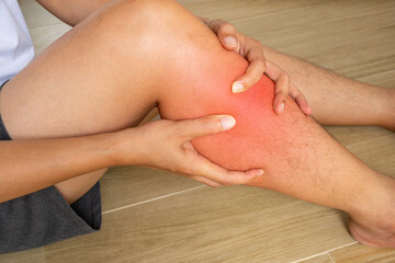Shin pain shown with hands supporting the lower leg and a red medical overlay. The image illustrates localized discomfort, inflammation and possible leg injury. © Prasert