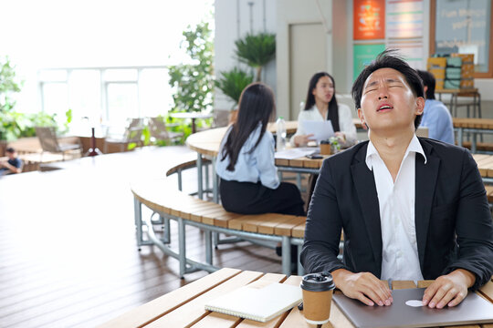 Stressed Asian Businessman Sitting at Outdoor Cafe with Eyes Closed