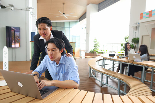 Two Asian Businessmen Collaborating on Laptop in Modern Outdoor Office Space