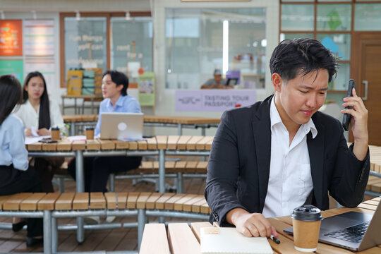 Asian Businessman Working on Laptop and Smartphone in Modern Outdoor Workspace