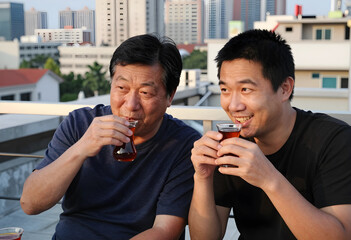 Obraz premium Intergenerational bonding and family connection, senior father and adult son drinking tea together on an urban rooftop terrace at sunset