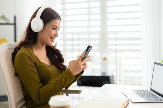 Relaxing Asian woman wear headphone listen to music or podcast select playlist on smartphone .