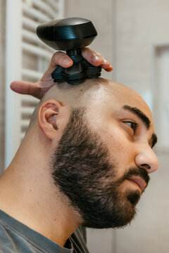 Close up of a young man shaving his head with an electric razor for head shaving in a bathroom. Head shaving with an electric head razor. A man shaving his head