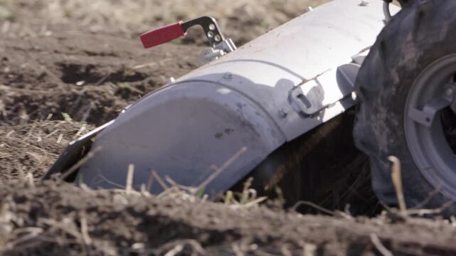 Farmer using rototiller machine to plow agricultural field soil for planting.