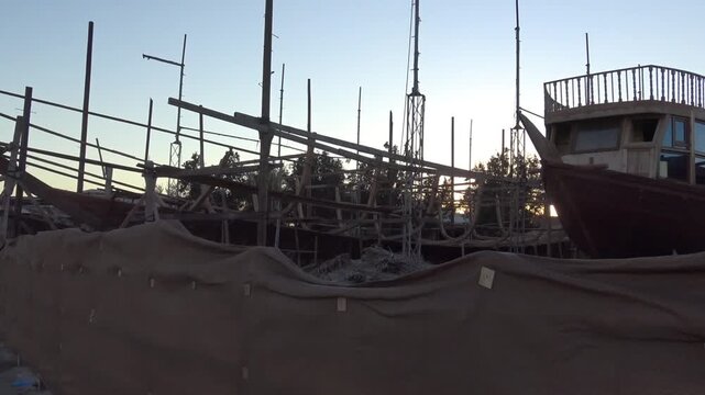 Traditional wooden dhow under construction at a shipyard at dusk, Sur, Oman