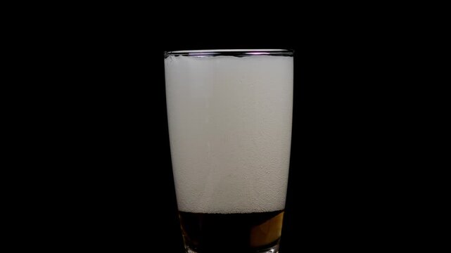 A glass filled with amber beer on black background.