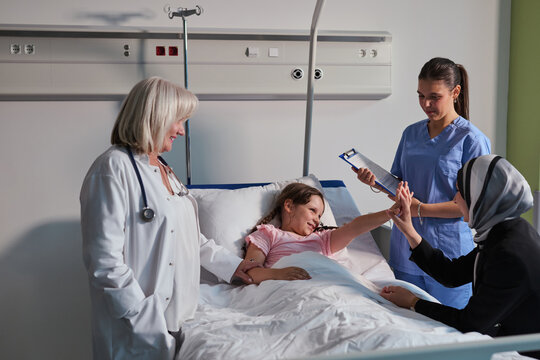 Medical team caring for young patient in hospital room while family offers support