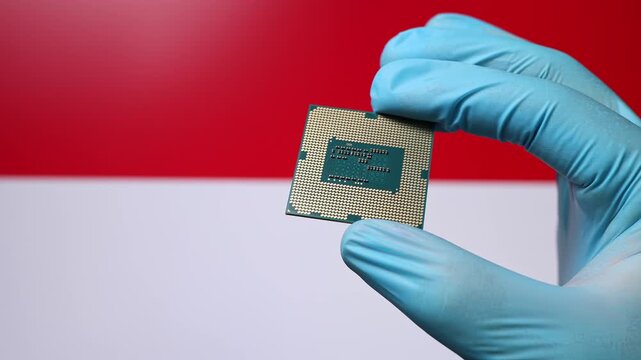 Close up view of hand in blue glove holding CPU microchip. Indonesian flag in blurred background. Concept of semiconductor shortage and artificial intelligence development in Indonesia.