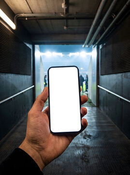 Hand holding a modern smartphone with a blank white screen in a stadium tunnel.