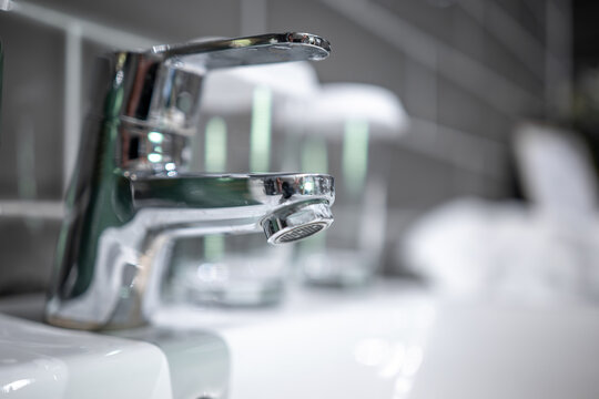 Close up of a modern chrome mixer tap on a white washbasin in a tiled bathroom