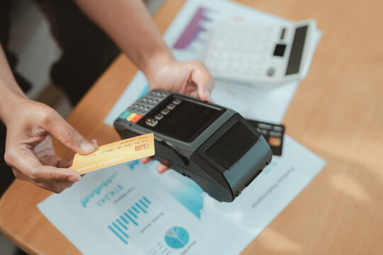 Financial advisor uses card payment terminal during wealth planning with printed business report and office paperwork on wooden desk for secure transaction and professional consultation