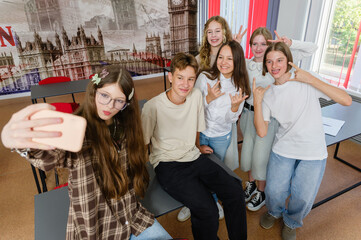 Obraz premium Group of teenage boys and girls take a fun selfie together while spending a break between lessons in the classroom.