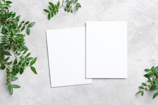 Two vertical blank cards mockup on a light concrete background, surrounded by fresh green foliage. Ideal for invitations, branding, and flyer presentations