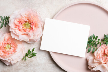 Horizontal blank white wedding card mockup on a round beige plate with peach roses and green leaves on a textured background. Elegant flat lay for invitations or greetings © nikavera