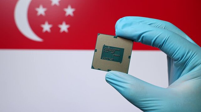 Close up view of hand in blue glove holding CPU microchip. Singaporean flag in blurred background. Concept of semiconductor shortage and artificial intelligence development in Singapore.