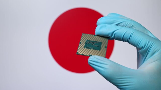 Close up view of hand in blue glove holding CPU microchip. Japanese flag in blurred background. Concept of semiconductor shortage and artificial intelligence development in Japan.