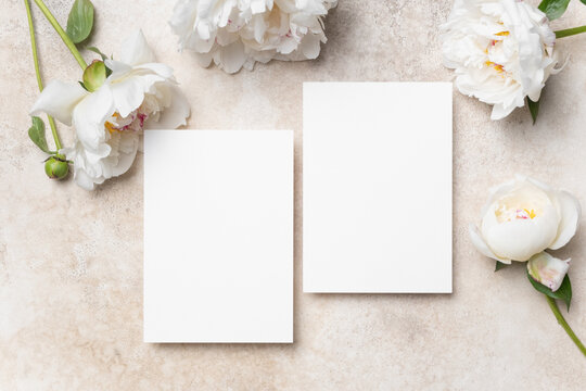 Blank wedding invitation mockup with copy space surrounded by delicate white peonies on a textured beige background, ideal for elegant greeting card designs