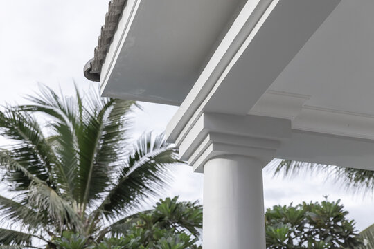 White classical column and porch eave framed by lush palm trees, conveying tropical coastal architecture, a relaxed resort atmosphere, elegant molding details and refined outdoor home exterior design