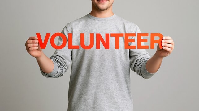 Young man holding volunteer text sign against gray background  