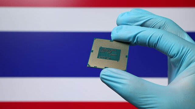 Close up view of hand in blue glove holding CPU microchip. Thai flag in blurred background. Concept of semiconductor shortage and artificial intelligence development in Thailand.