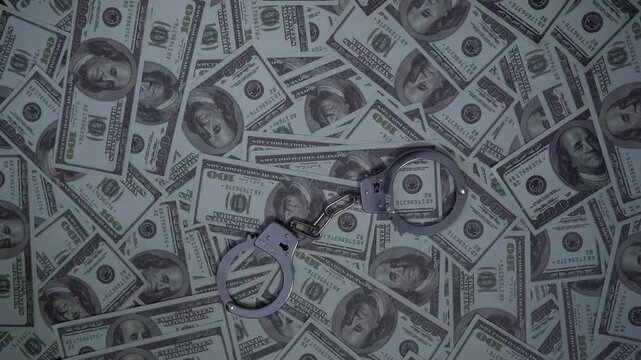 Metal handcuffs resting on top of stack of one hundred dollar bills.