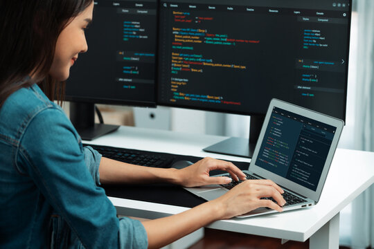Smiling young Asian in IT developer creating with typing online information on laptop with coding program data of application, wearing jeans shirt. surrounded by safety analysis two screen. Stratagem.