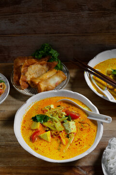 Creamy spicy Asian curry soup with tofu and vegetables, served with crispy spring rolls, pancakes, salad and chopsticks on a rustic wooden table.
