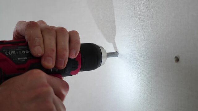 Worker drilling hole into white wall with cordless power drill, home repair process, renovation concept.
