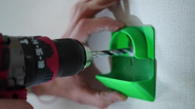Person drilling wall using electric drill with green dust collector accessory, dust free home repair, maintenance.