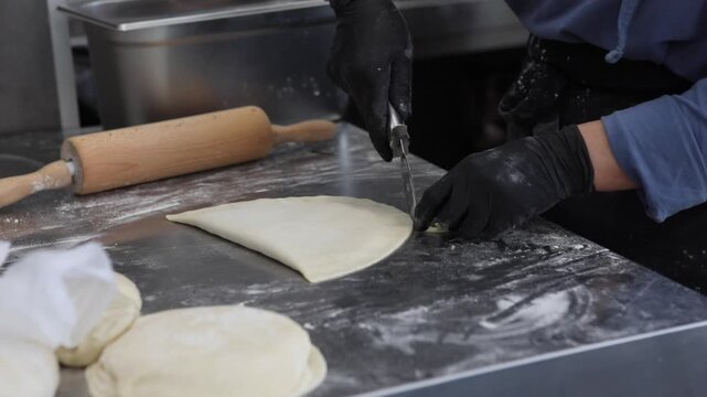 A female chef prepares traditional fried pastries in a professional restaurant kitchen, shaping dough and cooking fresh food by hand.