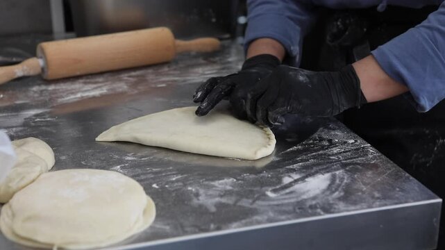 A female chef prepares traditional fried pastries in a professional restaurant kitchen, shaping dough and cooking fresh food by hand.