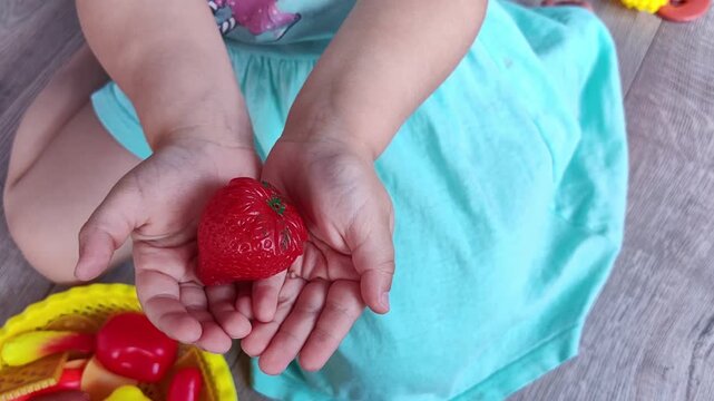 Child holds a red toy strawberry in both hands, colorful educational pretend play and imaginative childhood activity.