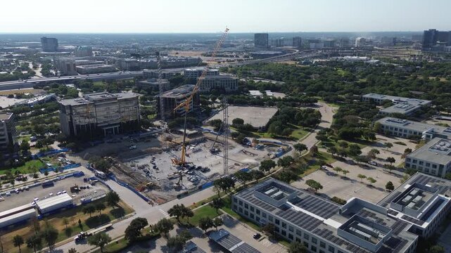 Tall lattice crane booms rise above excavated commercial foundations along Internet Blvd.. Active Hall Park job sites border photovoltaic office rooftops near Dallas North Tollway, Frisco, TX