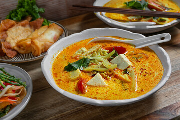 Creamy spicy Asian curry soup with tofu and vegetables, served with crispy spring rolls, pancakes,...