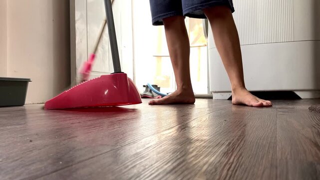 Slow motion low angle video of a housewife mopping a brown wooden floor with a purple mop. Close up view of daily household cleaning chores and domestic housework inside a home.