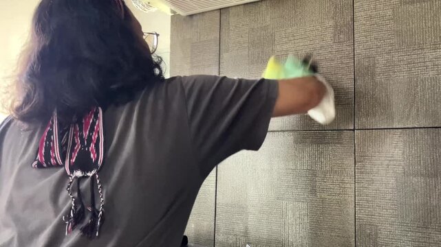 Slow motion video with selective focus of a housewife wearing rubber gloves. She is wiping and cleaning the dirty kitchen wall tiles with a sponge for daily domestic housework and hygiene.