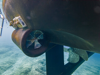 Close underwater view of yacht propellers, rudder and hull during marine inspection, revealing biofouling and maintenance needs in clear Mediterranean seawater with copy space © JairoMZ