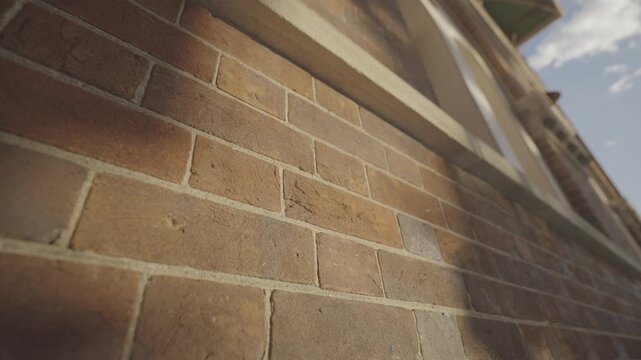 A close up view shows the textured sandstone brickwork of a heritage building wall lit by warm sunlight.