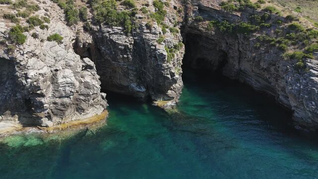Rugged vertical sea cliffs tower above crystal clear water, copy space