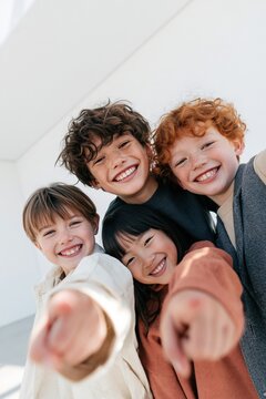 Happy diverse group of children laughing and pointing toward camera for kids background and classroom friendship scene in natural light