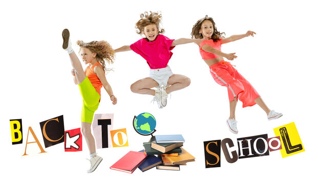Joyful girls leap above Back to School letters and classroom supplies. Concept of returning to school, study preparation, childhood joy, academic year, learning, and seasonal retail promotion.
