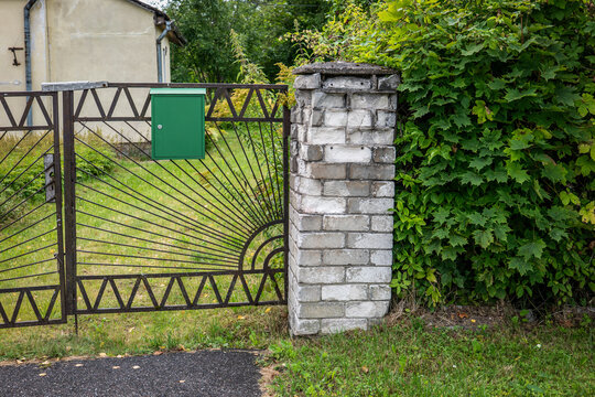 Green Mailbox on a Rustic Metal Gate Beside a Brick Pillar