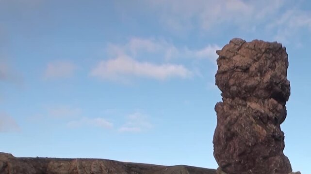 An awe-inspiring, craggy rock pillar dominates the landscape along the Arctic Ocean. Blue sky and scattered clouds frame this ancient, rugged landmark, a testament to extreme travel.