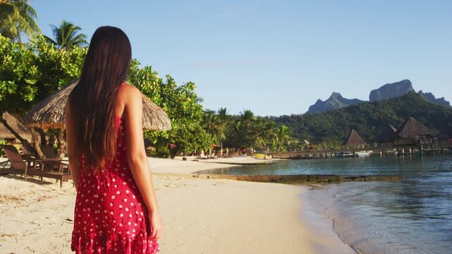 Beach vacation woman walking on Bora Bora island in Tahiti, French Polynesia at sunset with Mount Otemanu and overwater bungalows luxury hotel in the background. Raw video of real woman.