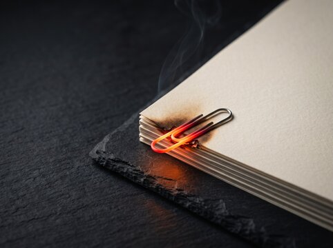 Glowing paperclip burning paper with smoke on dark background.