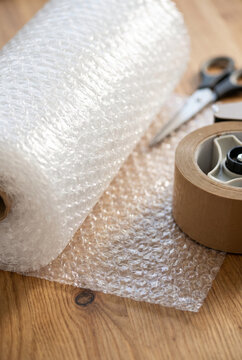 Clear bubble wrap roll and packing materials on wooden surface  